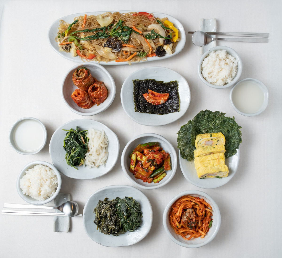 Assorted Side Dishes, Japchae, Mackgeolli and Rice on Table